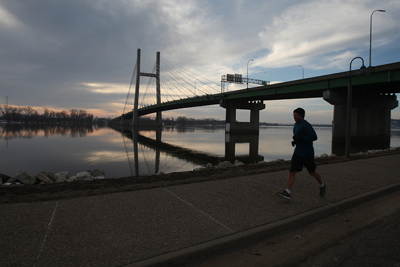 The sun rises behind a cloudy sky over the Great River Bridge and the Mississippi River making a scenic run for Don Schmidgall March 18, 2014 in Burlington. | John Gaines | The Hawk Eye